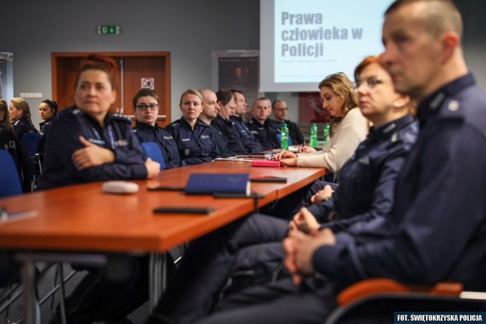 Policjanci siedzą przy stole podczas szkolenia. W tle rzutnik z napisem: "Prawa człowieka w Policji".