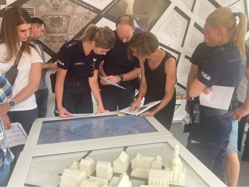 Grupa policjantek i policjantów w mundurach służbowych pochyla się nad gablotą w pawilonie "Muzeum na kółkach" w Świętochłowicach