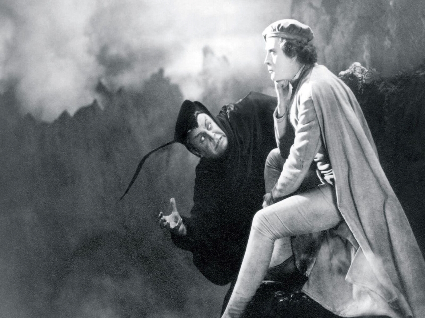 Kadr z filmu "Faust". Tytułowy bohater siedzi zamyślony, zza niego wyłania się Mefisto w czerni.