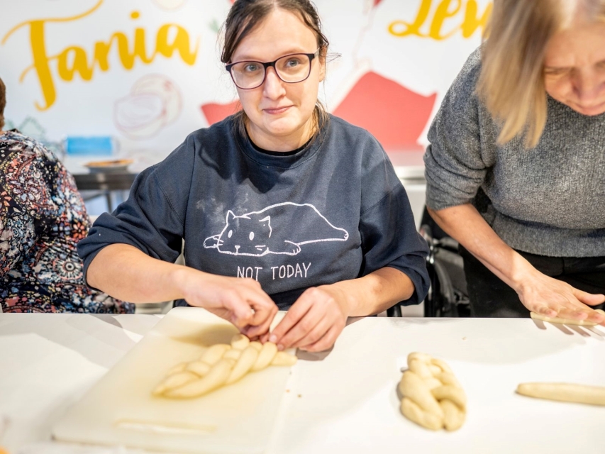 Dwie kobiety zaplatają chałkę podczas warsztatów kulinarnych w Muzeum POLIN.