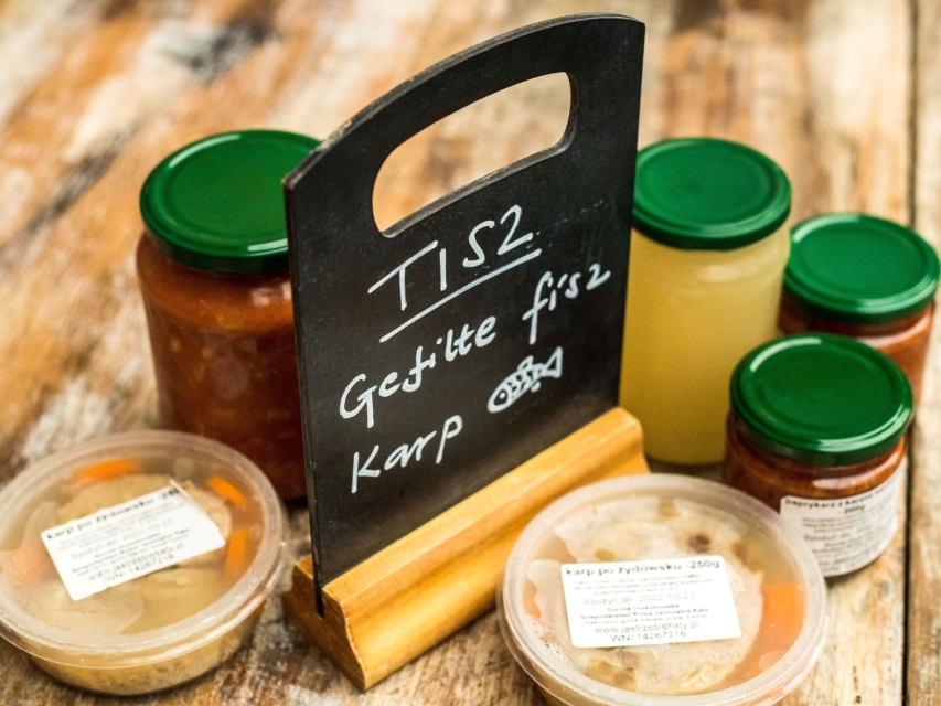 Przetwory w słoikach. Wokół nich tabliczka z napisem: TISZ, gefilte fisz, karp.