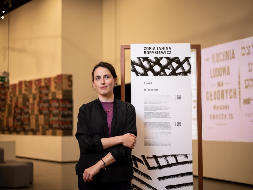 Zofia Janina Borysiewicz stoi przy stojaku z opisem jej pracy "Reprint".