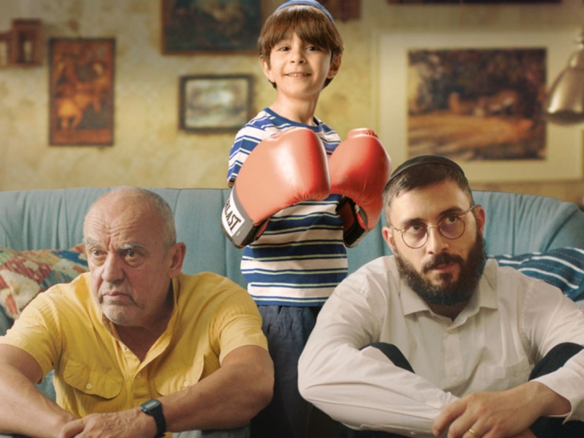 Kadr z filmu "Wszystko o Lewkowiczach". Na podłodze siedzą starszy i młodszy mężczyzna, a pośrodku nich stoi mały chłopiec w rękawicach bokserskich.
