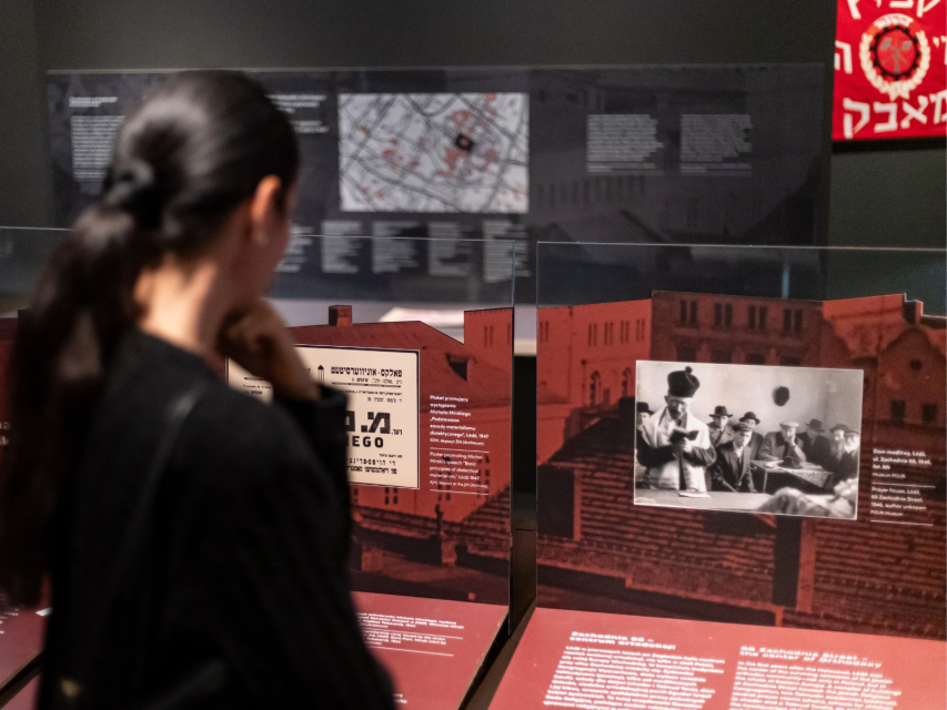 Kobieta zwiedza wystawę "1945. Nie koniec, nie początek". Ogląda zdjęcia i czyta opisy prezentowane w gablotach.