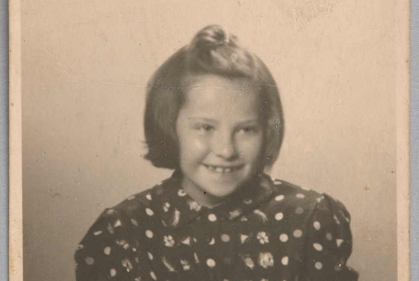 Zofia Zajczyk ubrana w koszulę kropki trzyma przed sobą książkę. Włosy ma rozpuszczone, a na czubku głowy zawiązany koczek.