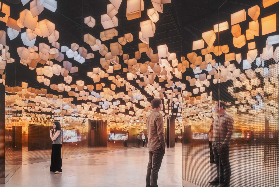 Three people are standing in the Bonds gallery. Colourful houses are hanging above them