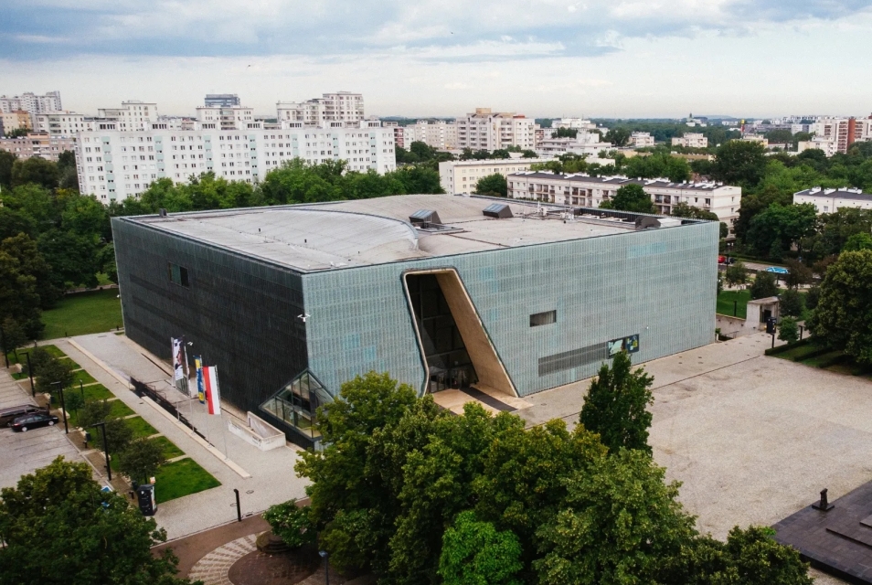 Budynek Muzeum POLIN z lotu ptaka. Otoczony zielonymi drzewami i blokami na Muranowie.