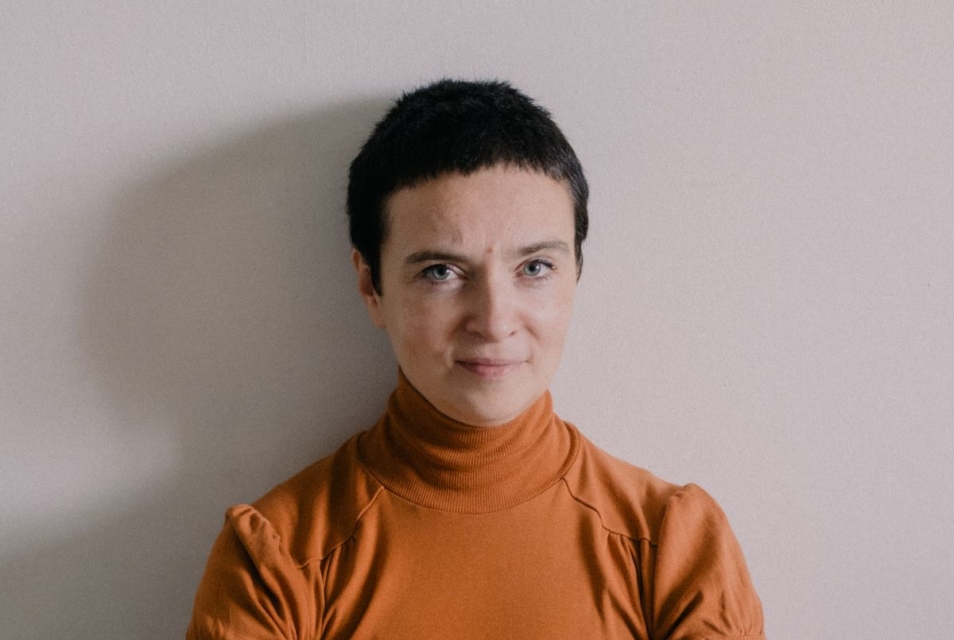 Patrycja Dołowy siedzi na podłodze, trzymając przed sobą splecione dłonie.