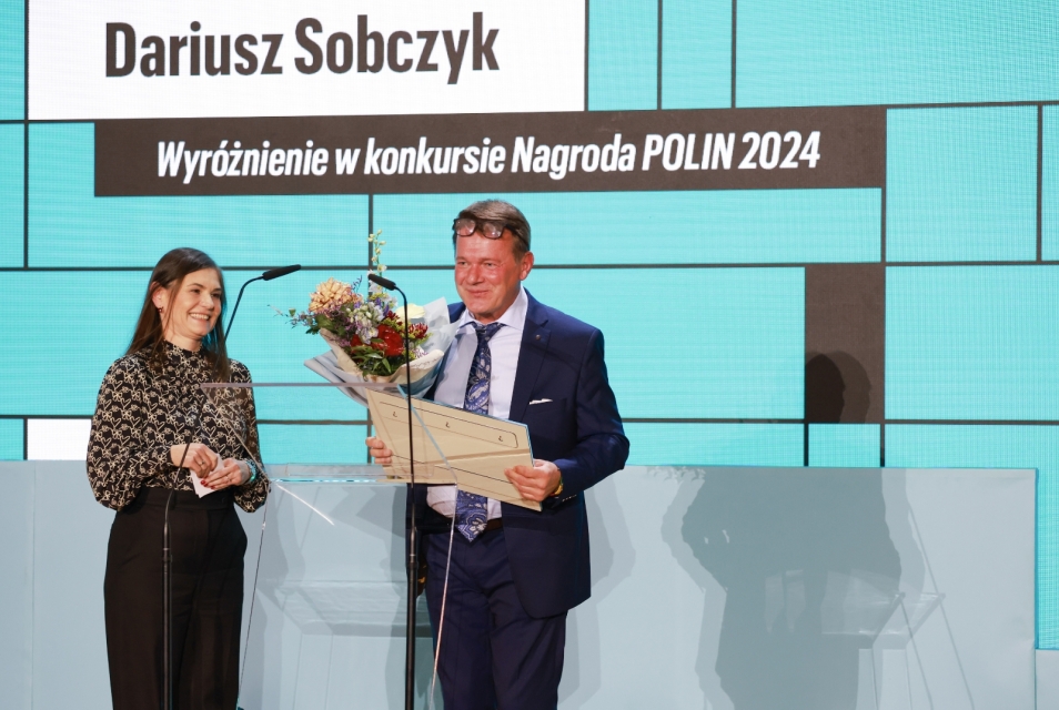 Standing on stage in the Auditorium are Dariusz Sobczyk and Łucja Koch.