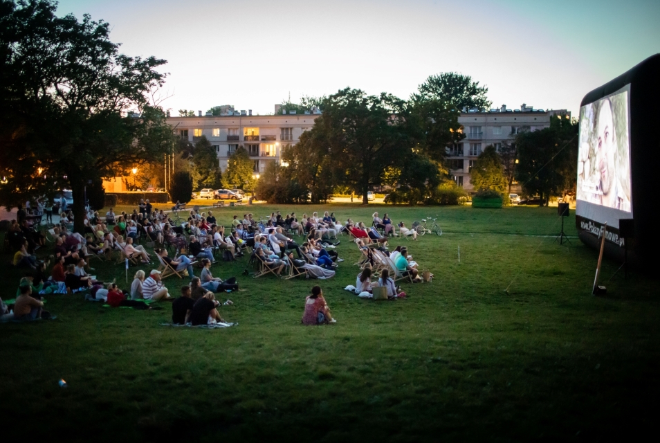Widzowie siedzą na rozkładanych leżakach, naprzeciwko nich, na ekranie wyświetla się film.