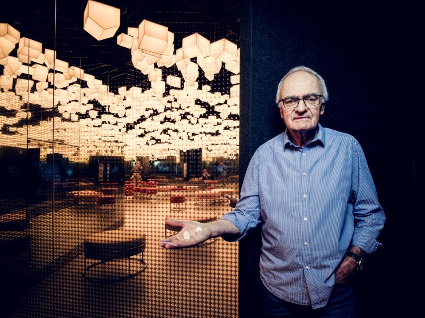 An elderly man poses in front of houses hanging from the ceiling in the Bonds gallery.