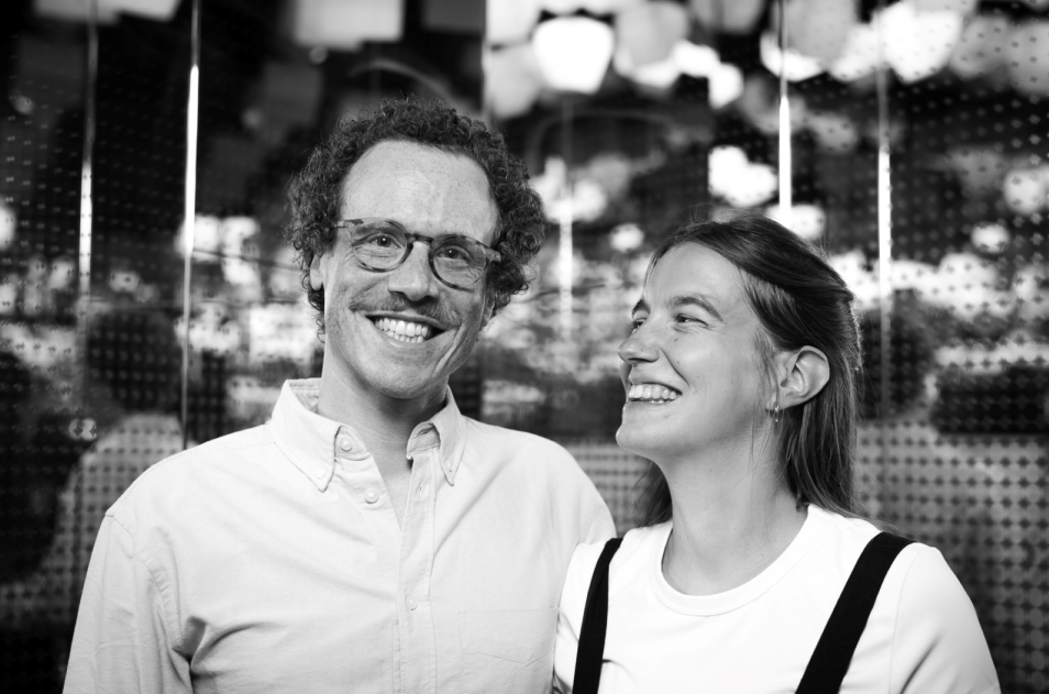 A laughing couple – a woman and a man. They pose in front of houses hanging from the ceiling in the Bonds gallery.