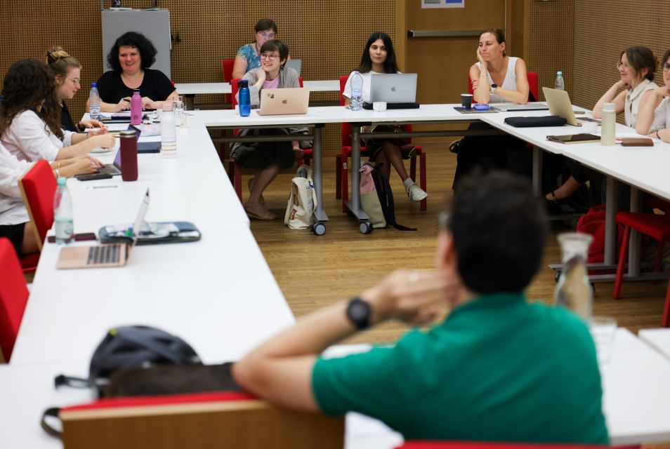 Uczestniczki i prowadzący Szkoły letniej siedzą przy stole w sali konferencyjnej.