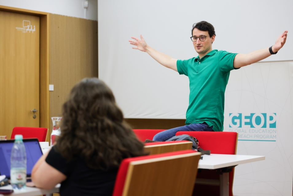 Prowadzący Szkoły letniej stoi z rękami uniesionymi po bokach.