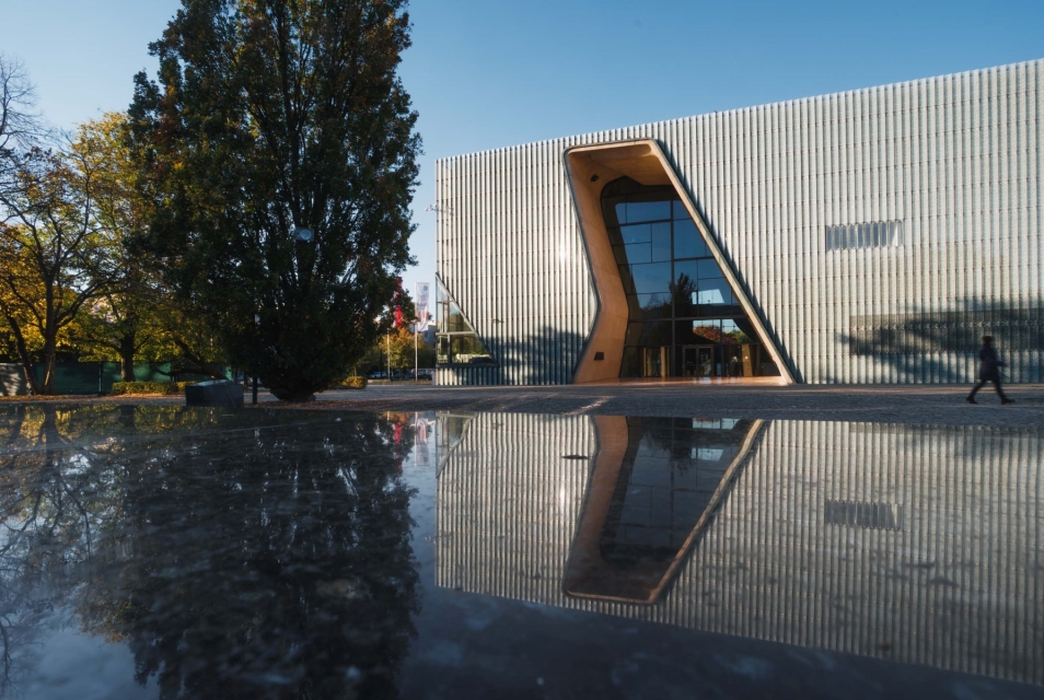 The POLIN Museum building is reflected in the surface of the Ghetto Heroes Monument.