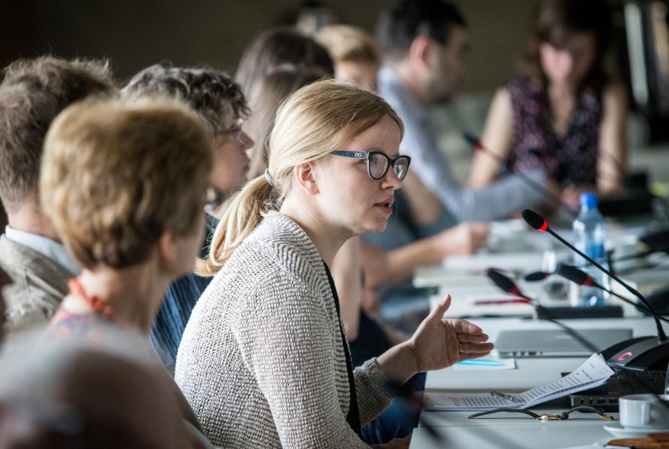 Participants of the scientific conference are seated at a table, next to microphones.
