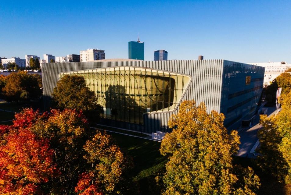 The POLIN Museum building surrounded by autumn trees with colourful leaves.