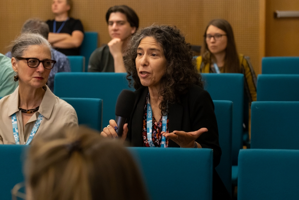 Several women are sitting in a room during a conference. One of them is holding a microphone.