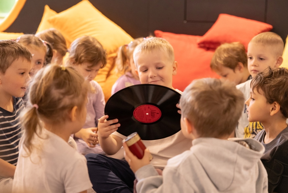 The boy is holding a vinyl record. Other children are sitting around him.
