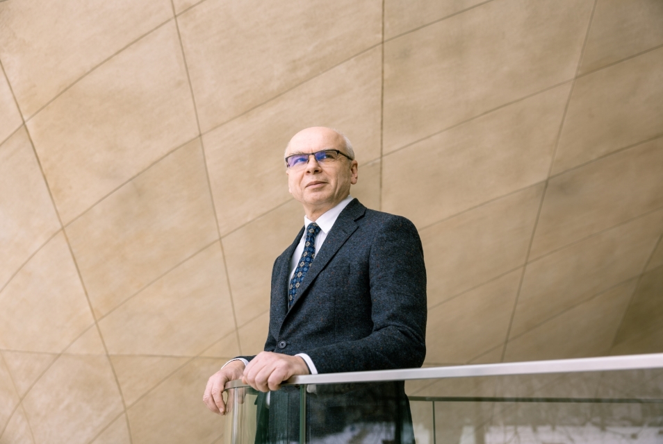 Dariusz Stola leans against the balustrade in the main hall of POLIN Museum. He looks to the side.