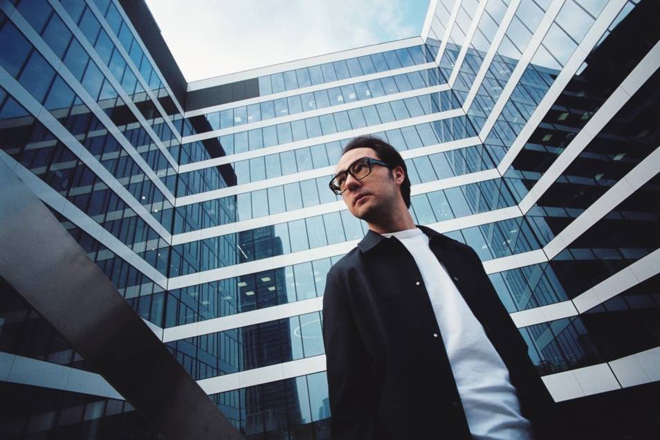 Aleksander Dębicz looks to the side. Behind him stands a glass skyscraper.