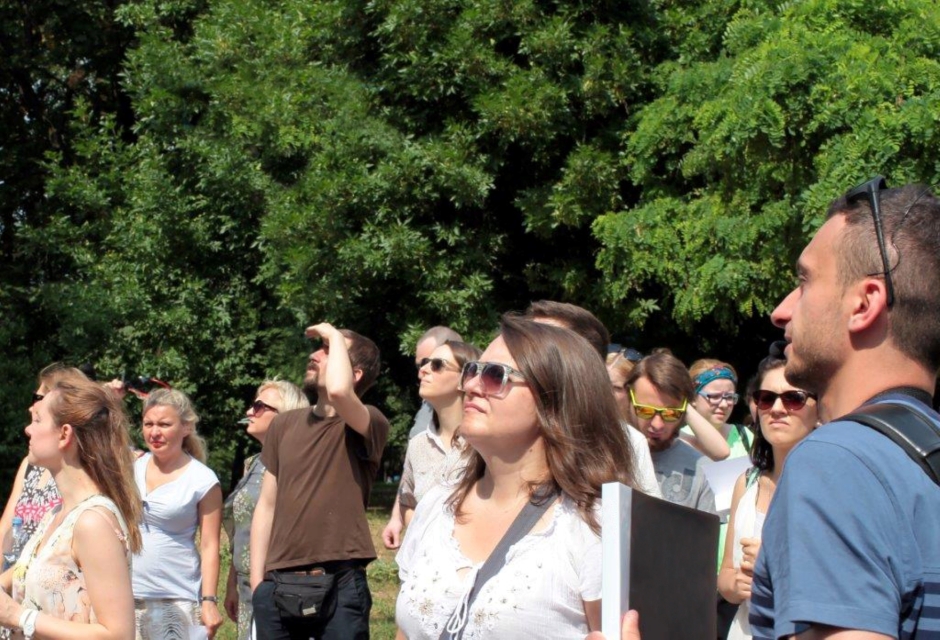 A group of women and men are looking to the side. Green trees in the background.