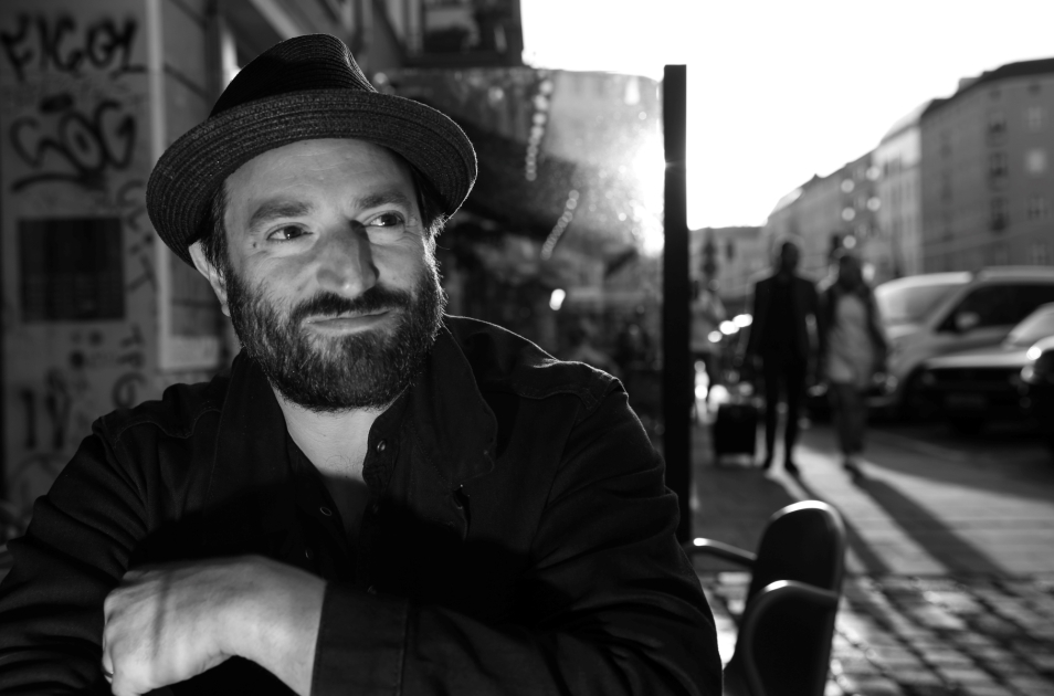Daniel Kahn w kapeluszu. W tle ulica w Berlinie.