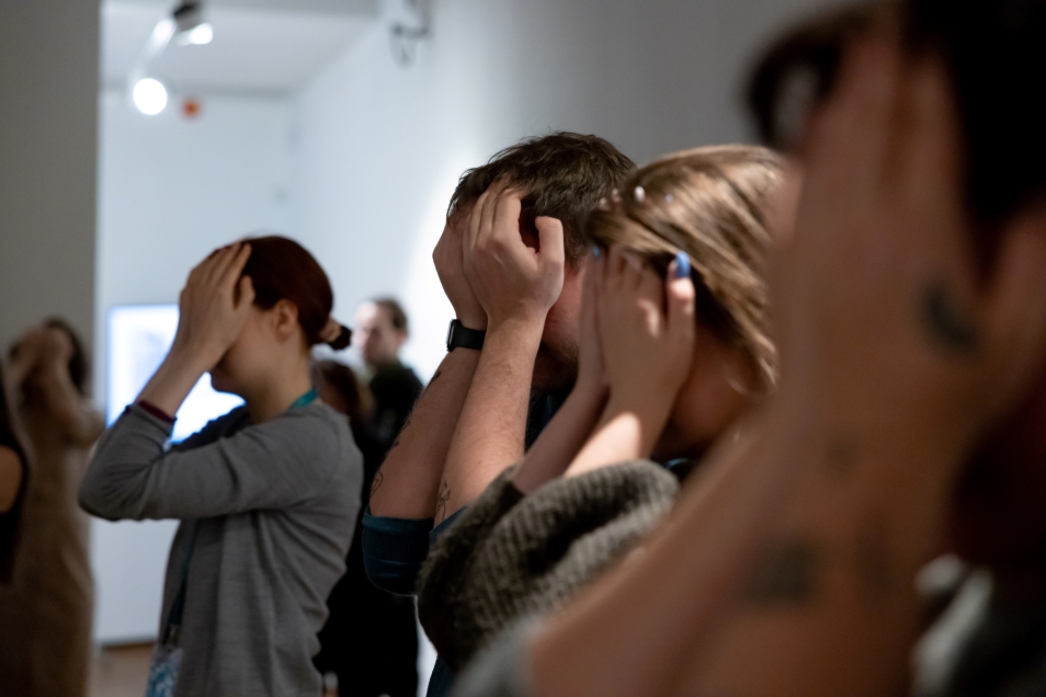 Several women are standing in a line, covering their eyes with their hands.