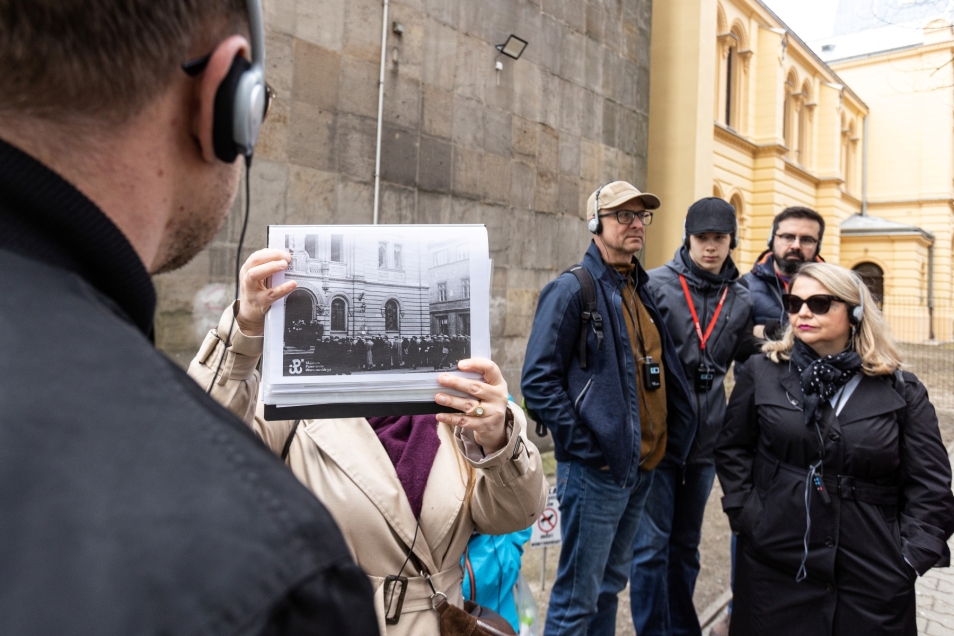 Przewodniczka pokazuje grupie archiwalne zdjęcie budynku podczas spaceru miejskiego po Warszawie.