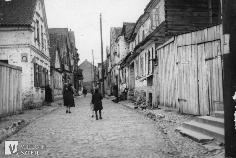 Białystok. Ulica w dzielnicy Chanajki przed 1939 rokiem. Po obu stronach stare kamienice z drewnianymi bramami. Na ulicy kilka osób w oddali.