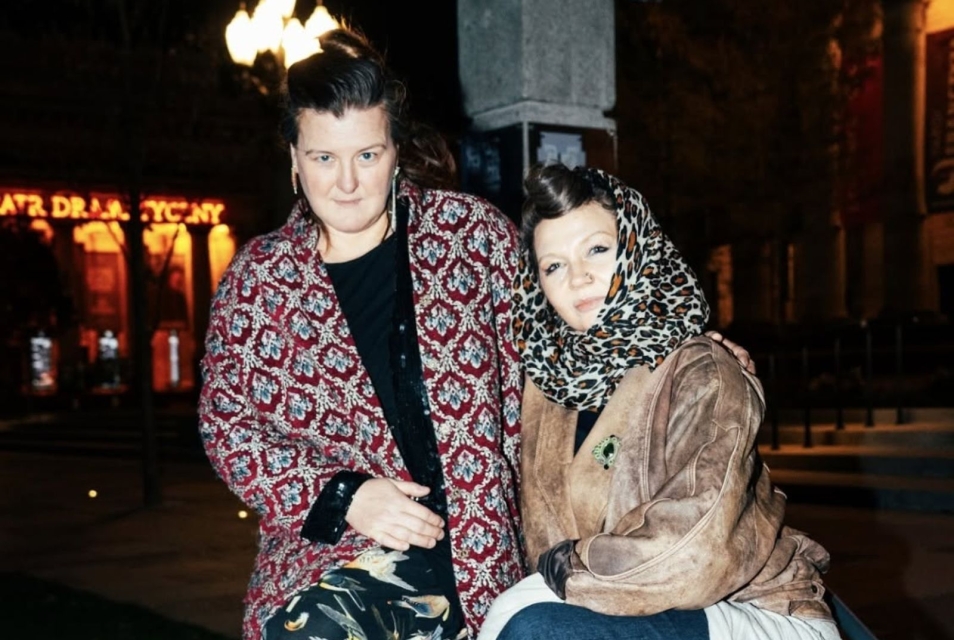 Dwie kobiety - Joanna Pawluśkiewicz i Aleksandra Markowska - ubrane w kolorowe tkaniny patrzą prosto w obiektyw.