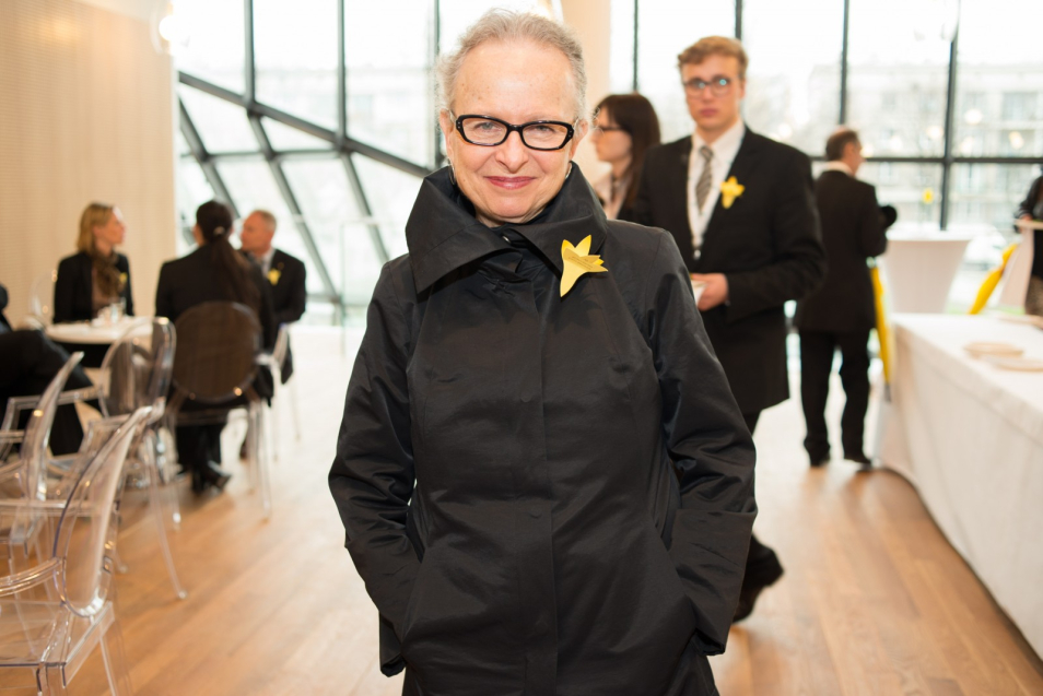 Barbara Kirshenblatt-Gimblett w holu Muzeum POLIN, do płaszcza ma przypięty papierowy żonkil.