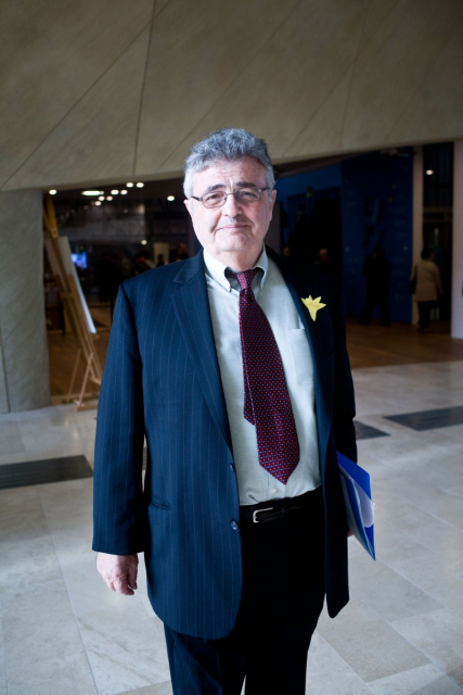 Mężczyzna w garniturze, do którego ma przypięty papierowy żonkil, stoi w holu Muzeum POLIN.