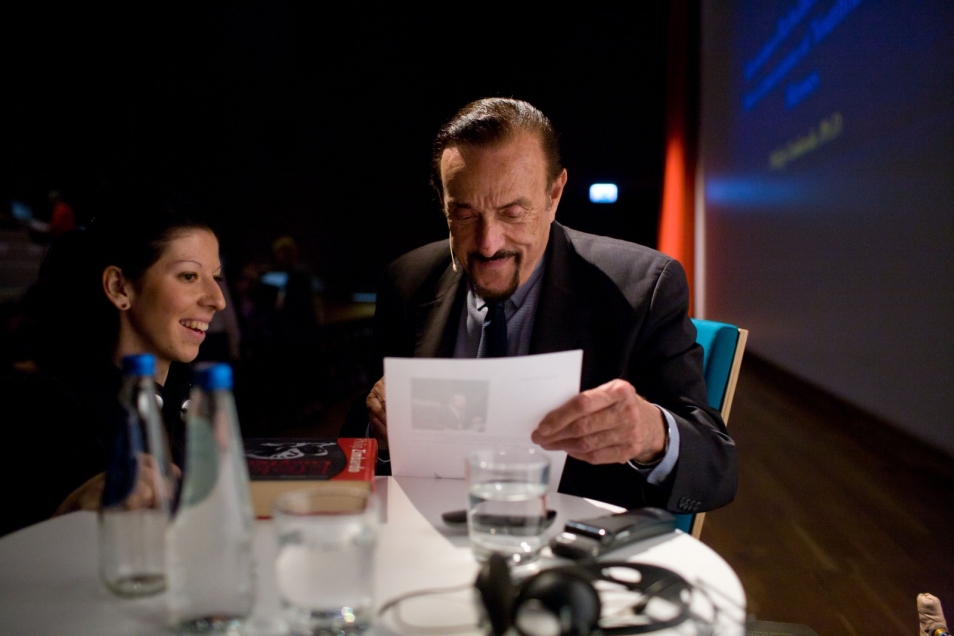 Uśmiechnięta kobieta siedzi obok Philipa Zimbardo.