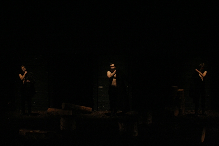 Trzej aktorzy na scenie podczas spektaklu "Utopia". Są prawie niewidoczni, na scenie jest ciemno.