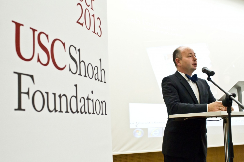Mężczyzna w garniturze mówi przez mikrofon podczas konferencji USC Shoah Foundation w 2013 r.