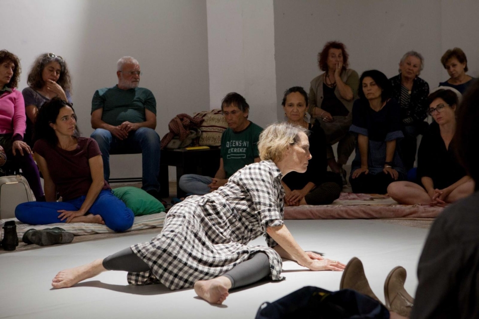 In between - performans Adiny Bar-On w Muzeum POLIN, Na zdjęciu: grupa kobiet i mężczyzn siedzi na podłodze pod ścianami pomieszczenia, na środku podłogi kobieta (Adina Bar-On) w trakcie performansu.