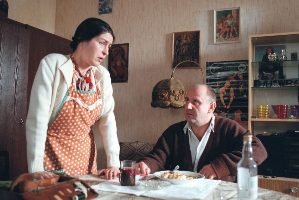 Kadr z filmu "Cud purymowy". Mężczyzna siedzi przy stole i rozmawia ze stojącą obok kobietą.