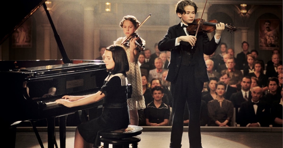 Cudowne dzieci (Wunderkind) - pokaz filmu w ramach WJFF, Na zdjęciu: kadr z filmu, przedstawia troje dzieci, które stoją na scenie i grają: dziewczynka na pianinie, chłopiec i druga dziewczynka na skrzypcach
