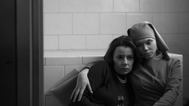 Czarno-biały kadr z filmu "Ida". Dwie kobiety, w tym tytułowa bohaterka, siedzą przytulone do siebie.