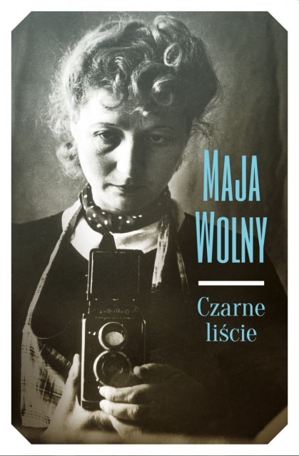 Okładka książki Mai Wolny - "Czarne liście". Kobieta w czarnej sukience patrzy lekko w dół, trzyma aparat.