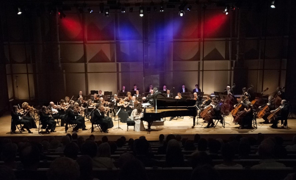 Koncert orkiestry symfonicznej. Solista gra na fortepianie, który stoi na środku sceny.