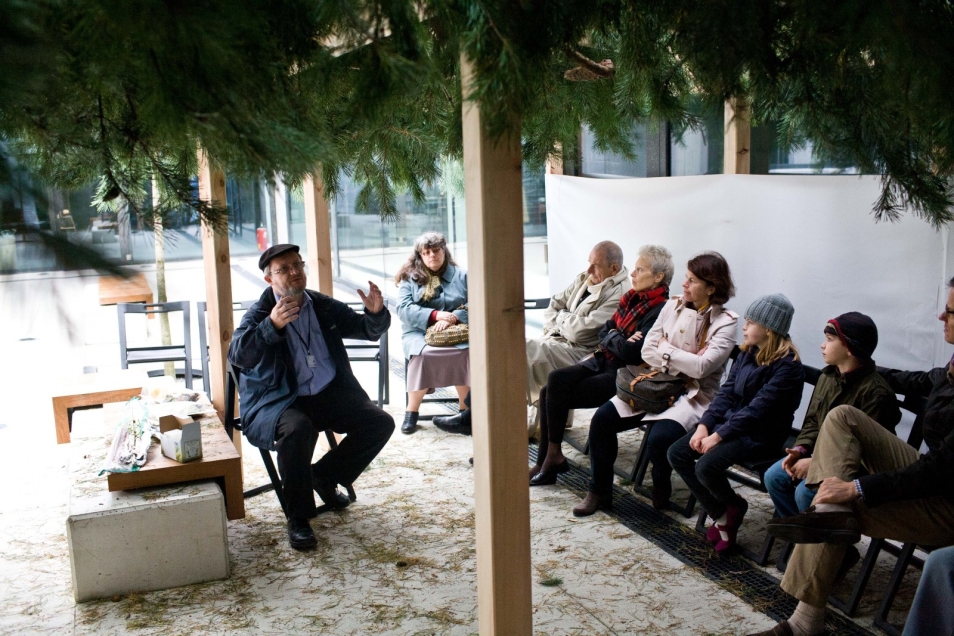 Kilka osób siedzi pod dachem szałasu budowanego na święto Sukkot.