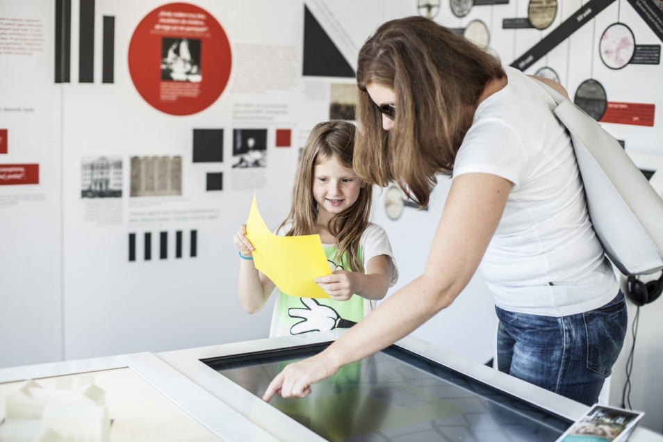 Dziecko z opiekunką w pawilonie Muzeum na kółkach. Cieszyn. Pochylają się nad gablotą wystawy.
