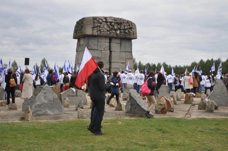 Mężczyzna z biało-czerwoną flagą stoi przy pomniku w Treblince.
