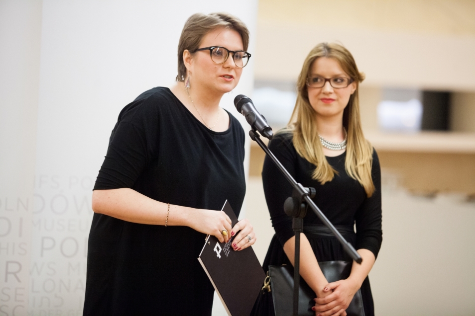 Dwie kobiety stoją przy mikrofonie podczas wernisażu wystawy o Sprawiedliwych.