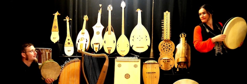 Na ścianie wiszą instrumenty. Mężczyzna i kobieta, stojący w dwóch przeciwległych częściach pomieszczenia, patrzą na siebie..