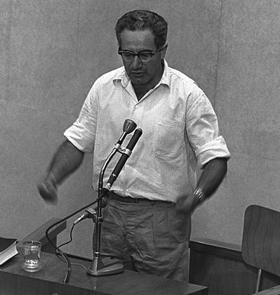 Israel Guttman. Czarno-białe zdjęcie przedstawia stojącego mężczyznę w białej koszuli.