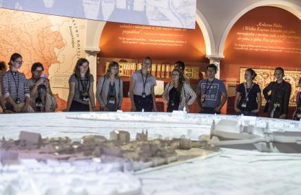 Grupa młodzieży stoi przed ogromną, podświetloną makietą średniowiecznego Krakowa. W tle ściany wystawy "1000 lat historii Żydów polskich" Muzeum POLIN