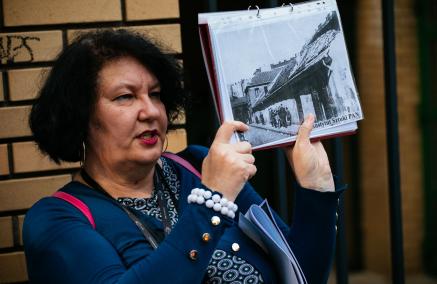 Przewodniczka Katarzyna Jakubowicz prezentuje archiwalne zdjęcie podczas spaceru miejskiego.